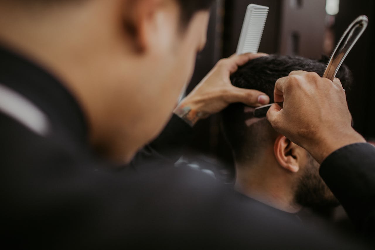 Barberia Unisex Cesar. Close-up of a barber expertly styling a mans hair with a razor and comb in a trendy barbershop.